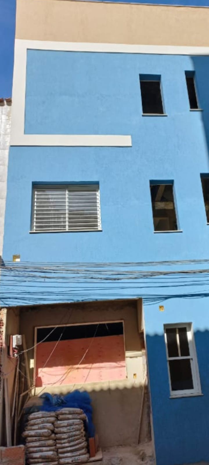 Fachada de prédio pintada de azul com sacos de cimento no térreo